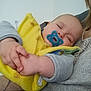 baby, child, closed_eyes, cozy, cute, grey_sleeves, hand, holding, indoor, infant, knitted_sweater, nap, pacifier, peaceful, person, portrait, resting, sleeping, soft_light, yellow_bib