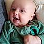 baby, infant, smiling, green_onesie, fist, couch, cushion, face, person, happy, indoor, head, skin, sitting, cute, expression, portrait, young_child, clothing, cozy