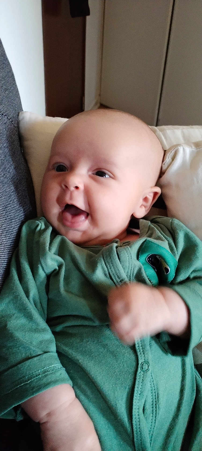 Livio participe au concours pour gagner de l'argent avec cette photo : baby, infant, smiling, green_onesie, fist, couch, cushion, face, person, happy, indoor, head, skin, sitting, cute, expression, portrait, young_child, clothing, cozy