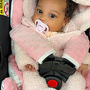 Sanovia is registered to the contest to win money with this photo: adorable, baby, big_eyes, blanket, buckle, car_seat, close_up, cozy, curly_hair, fingers, hood, infant, jacket, pacifier, pink, portrait, safety_belt, seat_padding, soft_texture, strap
