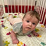 baby, bedding, child, clothing, colorful, crib, cute, eyes, face, fingers, flower_pattern, gray_shirt, hand, indoors, infant, letters, pink_pants, red_background, tummy_time, wooden_bars