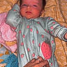 baby, infant, onesie, strawberry_pattern, hand, quilt, blanket, sleepy, lying_down, child, comfort, soft_toy, pink, yellow, blue, patterned_fabric, cute, indoors, portrait, skin