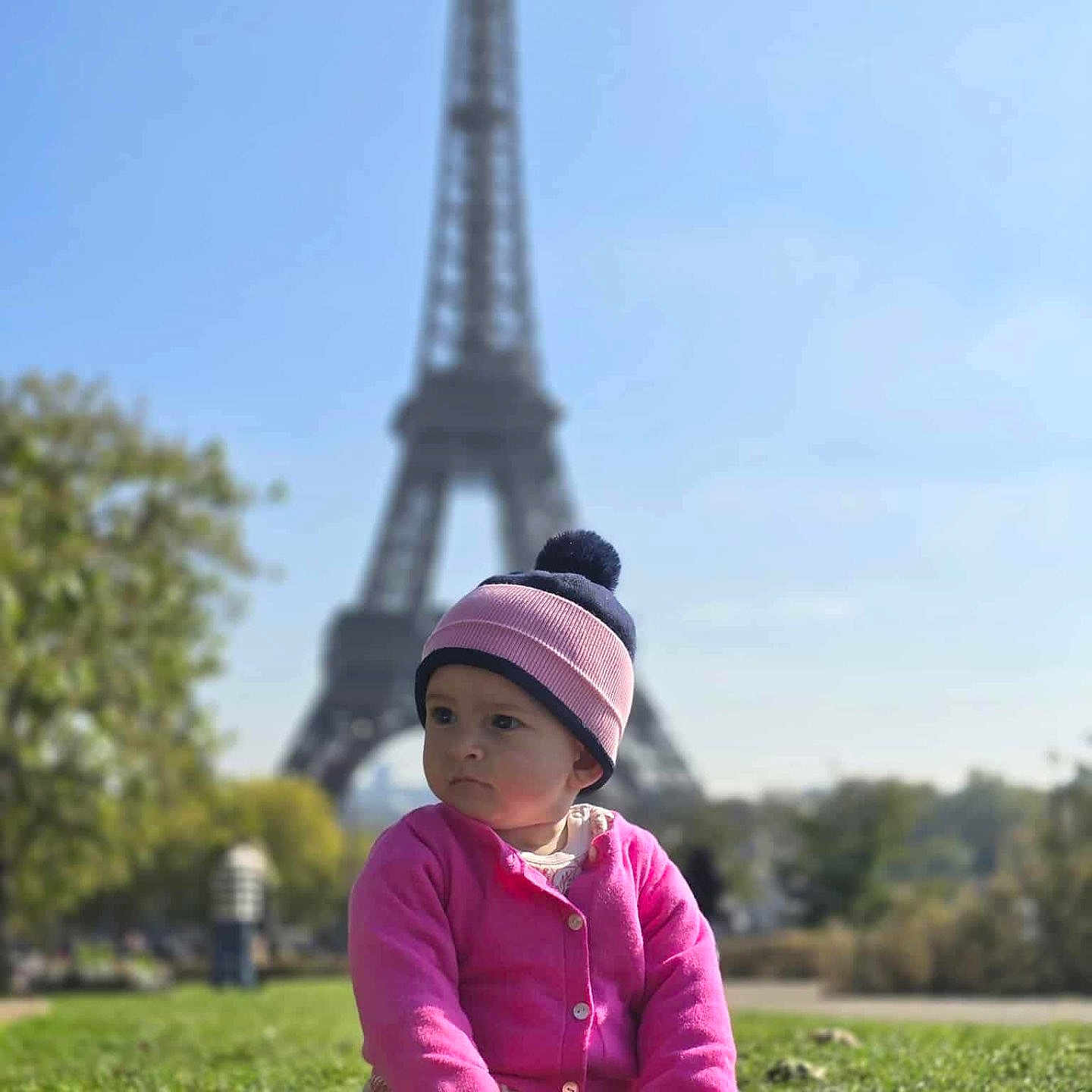 Lynda-Rose participe au concours pour gagner de l'argent avec cette photo : casual_clothing, child, cute, daylight, eiffel_tower, grass, hat, landmark, nature, outdoor, park, person, pink_sweater, portrait, shoes, sitting, sky, toddler, trees, urban