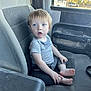 toddler, child, car_seat, barefoot, gray_clothing, blue_eyes, curious, indoor, vehicle_interior, window, plastic_bag, paper, seat, dusty, young_child, person, sitting, expression, casual, portrait