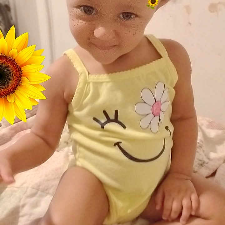 Nova is registered to the contest to win money with this photo: baby, bed, child, curly_hair, cute, face, feet, flower_design, freckles, hand, happy, indoor, playful, portrait, sitting, skin, smiling, sunflower_filter, toddler, yellow_onesie