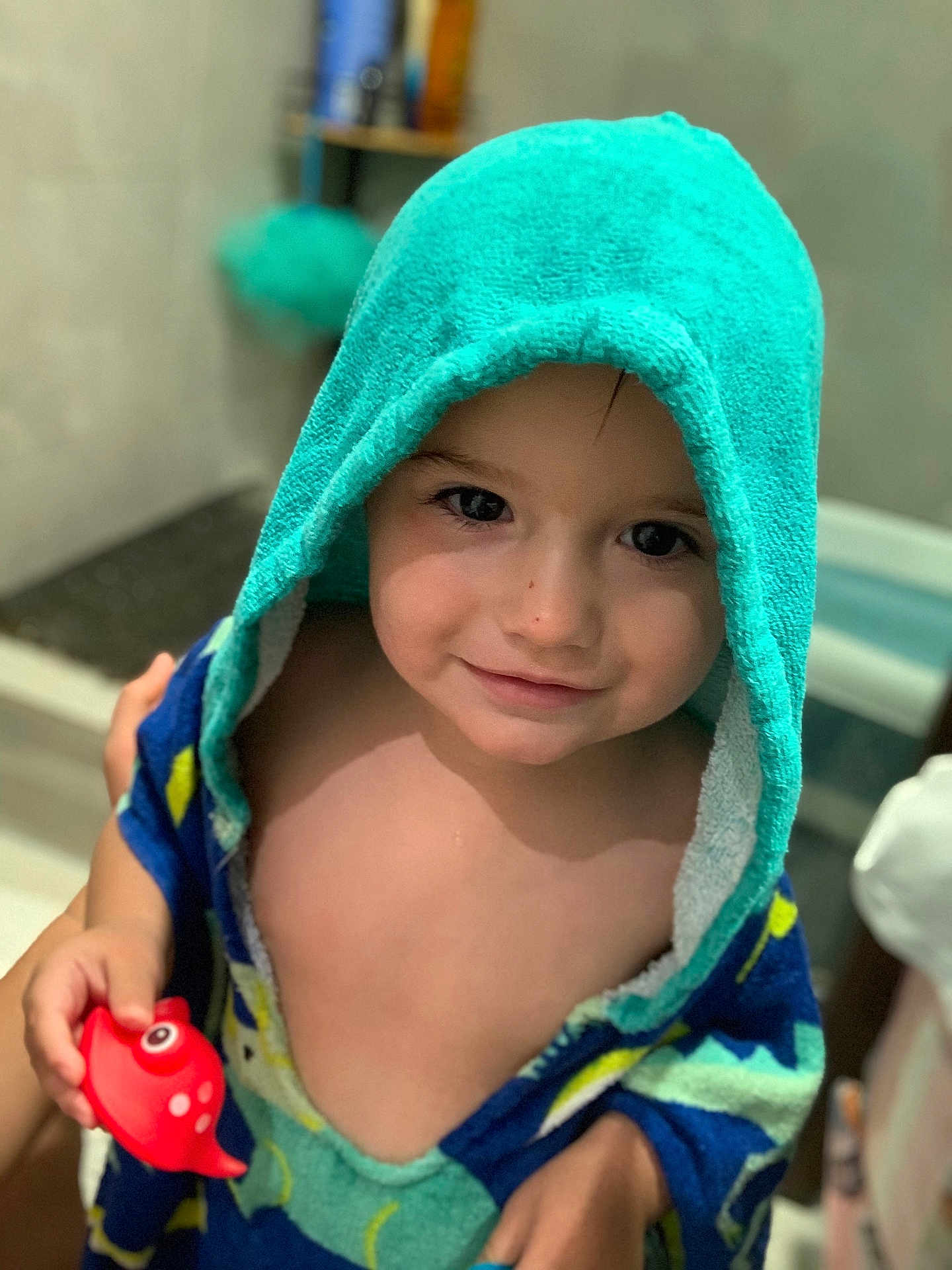 Gabriel a rejoint le concours — aidez-le/la à gagner de superbes lots ! child, toddler, towel, hooded_towel, bathroom, toy, red_toy, fish_toy, smile, face, skin, hand, cute, indoor, person, young_child, play, happy, portrait, water