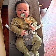 Carmine is registered to the contest to win money with this photo: baby, baby_bouncer, blanket, child, comfort, cute, drawer, face, floor, footwear, furniture, green_clothing, hand, home, indoor, infant, pacifier, sitting, straps, wood_floor