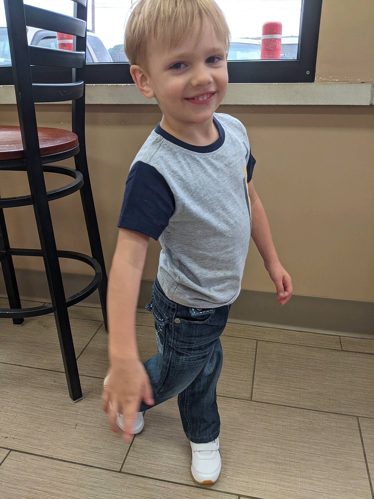 Noah is registered to the contest to win money with this photo: child, chin, denim, floor, flooring, fun, hair, jeans, joint, joy, knee, leg, person, sleeve, smile, standing, t_shirt, television, toddler, trunk