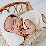baby, sleeping, newborn, infant, knit_hat, white_clothing, wicker_basket, blanket, pillow, cozy, peaceful, cute, soft_texture, resting, portrait, indoors, child, toddler, hands, face