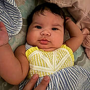 Ana Victoria is registered to the contest to win money with this photo: baby, infant, child, face, hand, clothing, striped_dress, yellow, blue, bed, pillow, blanket, cute, chubby_cheeks, portrait, indoor, person, skin, fingers, lying_down