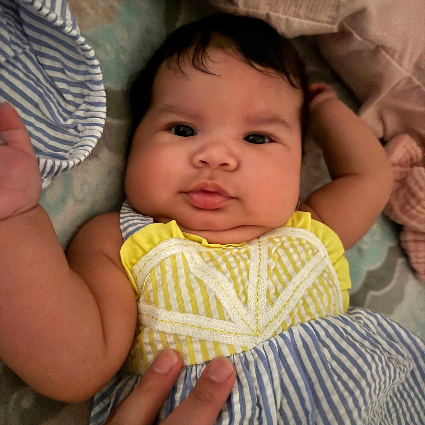 Ana Victoria is registered to the contest to win money with this photo: baby, infant, child, face, hand, clothing, striped_dress, yellow, blue, bed, pillow, blanket, cute, chubby_cheeks, portrait, indoor, person, skin, fingers, lying_down