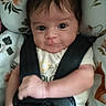baby, infant, car_seat, safety_harness, floral_pattern, clothing, cute, face, expression, child, seat, strapped_in, adorable, young, person, indoor, portrait, holding, hands, smile