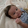 éden is registered to the contest to win money with this photo: baby, bed, blanket, child, clothing, cozy, cute, eyes, face, hair, hand, indoors, infant, lying_down, onesie, photography, portrait, relaxed, smiling, soft