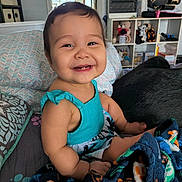 Mariana joined the competition — help win amazing prizes! baby, child, smiling, sitting, dress, blanket, pillow, bed, indoor, room, toy, stuffed_animal, shelf, mirror, happy, person, face, hair, skin, home