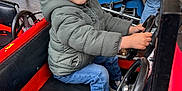 Pablo participe au concours pour gagner de l'argent avec cette photo : child, smiling, carousel, ride, car, steering_wheel, beanie, puffy_jacket, jeans, sneakers, red_car, seat, happy, playful, amusement_park, candid, portrait, family_fun, outdoor, metal_rail
