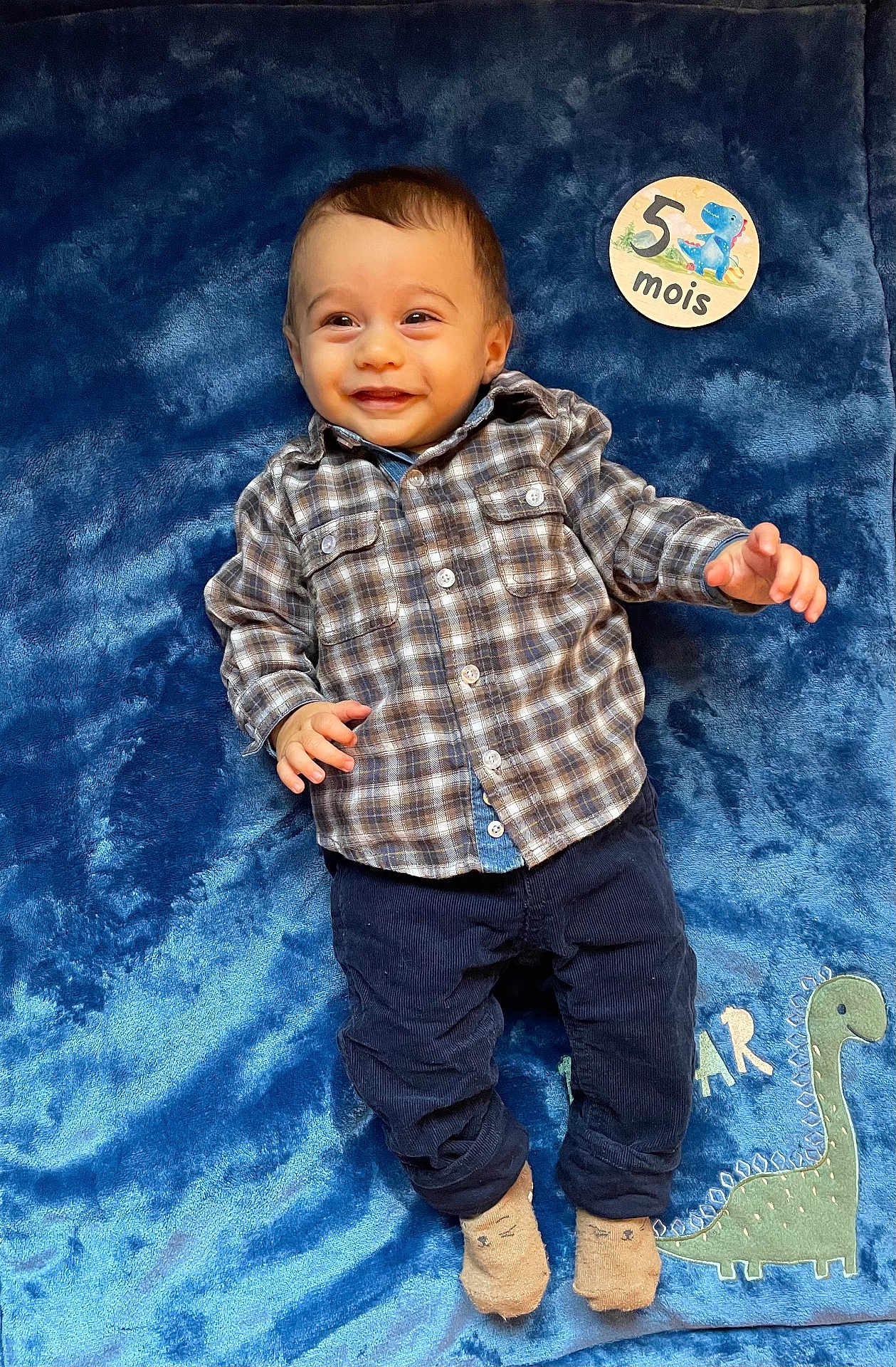 Arthur a rejoint le concours — aidez-le/la à gagner de superbes lots ! baby, child, smiling, plaid_shirt, navy_pants, blue_blanket, dinosaur, socks, infant, portrait, cute, lying_down, happy, clothing, soft_texture, indoor, person, five_months, sign, adorable