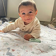 Arthur a rejoint le concours — aidez-le/la à gagner de superbes lots ! baby, child, infant, smile, face, eyes, blanket, dinosaur_print, sweater, hand, lying_down, indoors, soft_light, cute, portrait, young_child, cozy, happy, playful, bedroom