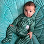 baby, infant, green_onesie, striped_clothing, plush_cushion, turquoise, child, portrait, indoor, cute, looking_at_camera, soft_fabric, comfortable, small_hand, footed_pajamas, young_child, adorable, seated, baby_face, cozy