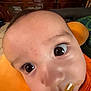 baby, close_up, face, drool, orange_clothing, orange_cushion, curious, wide_eyes, indoor, wooden_cabinet, furniture, child, person, portrait, skin, head, expression, young_child, infant, resting