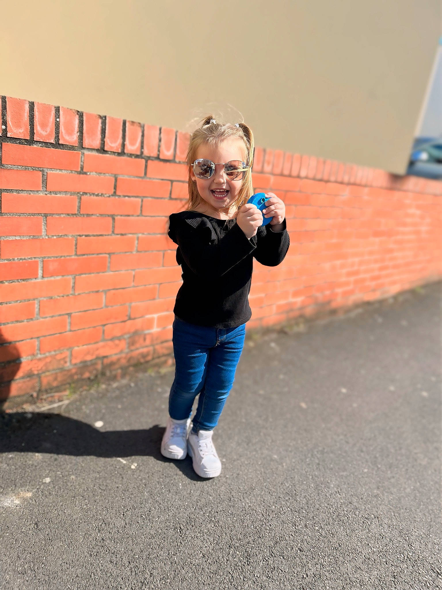 Naelys participe au concours pour gagner de l'argent avec cette photo : asphalt, child, city, denim, electric_blue, eyewear, flooring, fun, gesture, happy, leisure, person, recreation, road_surface, shadow, sitting, smile, standing, t_shirt, toddler
