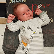 Tylio a rejoint le concours — aidez-le/la à gagner de superbes lots ! baby, child, infant, onesie, striped_clothing, giraffe_design, pillow, text_on_pillow, bed, sleepwear, relaxed, indoor, cute, human, face, hands, lying_down, cozy, soft_lighting, portrait