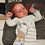 baby, child, infant, onesie, striped_clothing, giraffe_design, pillow, text_on_pillow, bed, sleepwear, relaxed, indoor, cute, human, face, hands, lying_down, cozy, soft_lighting, portrait