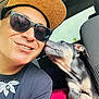 Mana is registered to the contest to win money with this photo: man, dog, puppy, selfie, car, hat, sunglasses, smile, pet, red_blanket, interior, seat, necklace, black_shirt, closeup, friendship, cute, animal, companion, affection