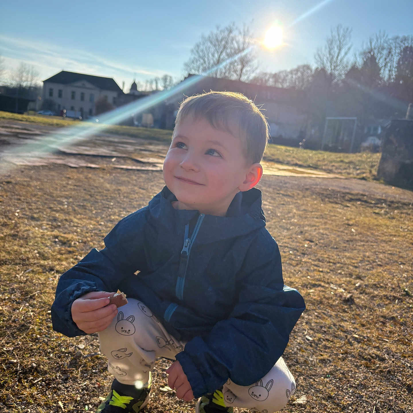 Sohann participe au concours pour gagner de l'argent avec cette photo : child, boy, outdoor, sunlight, sunflare, jacket, pants, sneakers, grass, sky, smile, face, daylight, nature, crouching, snack, happy, casual_clothing, playful, young
