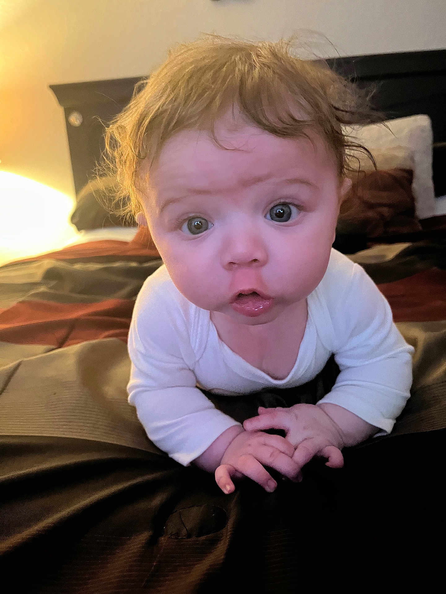 Victoria is registered to the contest to win money with this photo: baby, infant, child, bed, blanket, white_clothing, hands, face, eyes, curly_hair, expression, indoor, bedroom, pillow, headboard, soft_lighting, closeup, person, skin, cute