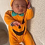 baby, infant, sleeping, pumpkin_costume, orange_clothing, hat, cute, child, costume, face, hand, footed_pajamas, indoors, resting, soft_texture, cozy, lying_down, peaceful, young_child, portrait