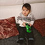 Ahyann-Mathïs participe au concours pour gagner de l'argent avec cette photo : black_hair, child, clothing, couch, cozy, curious, cute, furniture, home, indoor, jeans, person, pillow, play, portrait, sitting, smile, sweater, toddler, toy_car