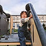 Ahyann-Mathïs participe au concours pour gagner de l'argent avec cette photo : child, toddler, playground, climbing, denim_overalls, sneakers, curly_hair, tongue_out, outdoor, urban, steps, metal, wood, building, sky, cloudy, fun, play, cute, person