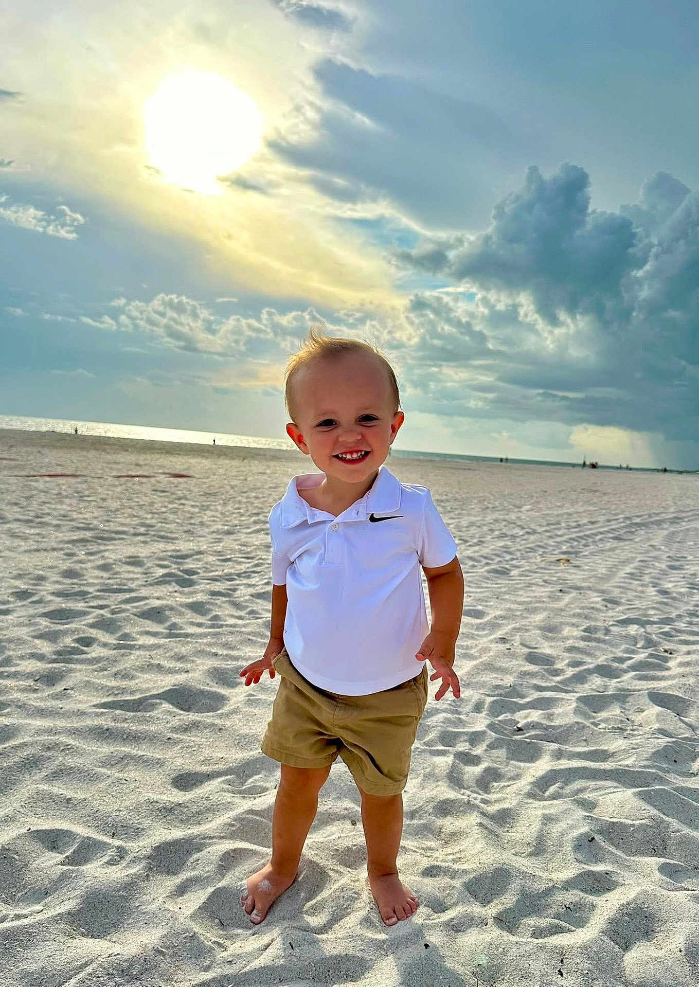 Tate is registered to the contest to win money with this photo: child, toddler, beach, sand, sunlight, clouds, sky, smile, barefoot, shorts, polo_shirt, outdoor, summer, sun, happy, vacation, nature, standing, portrait, casual_clothing