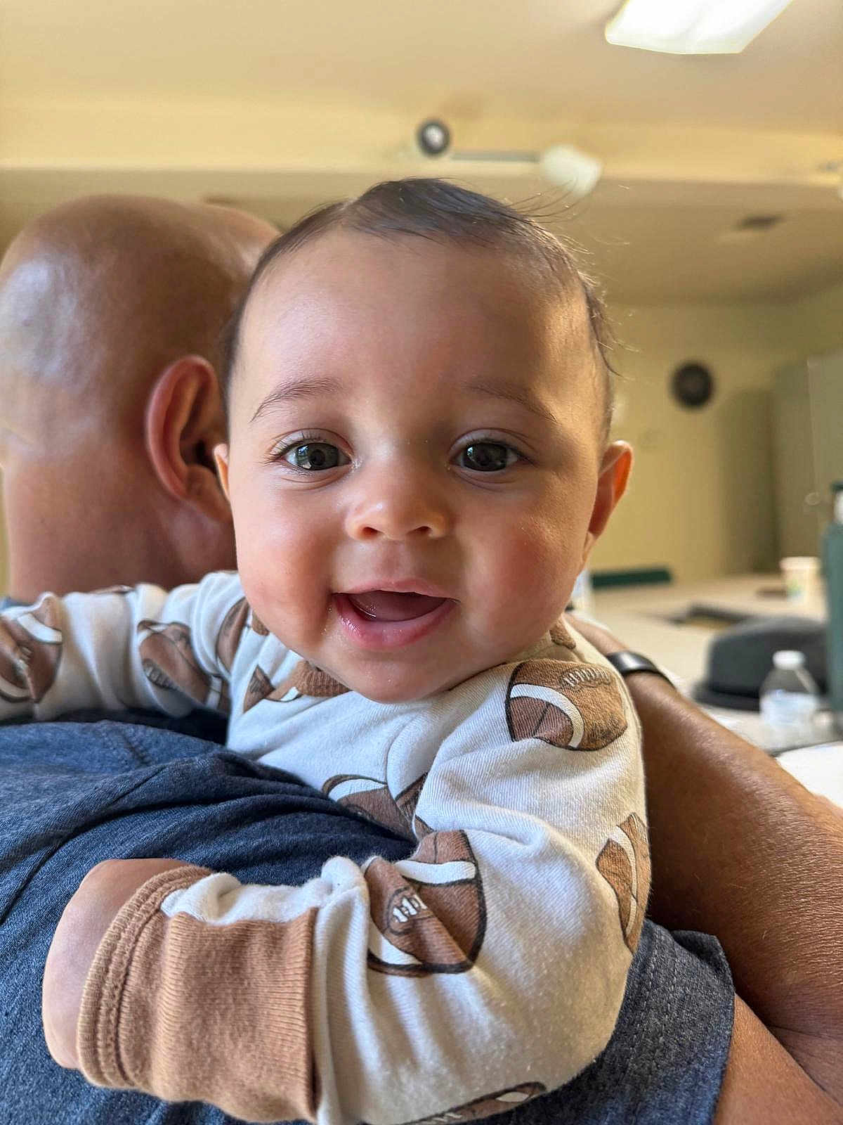 Roman joined the competition — help win amazing prizes! baby, child, smiling, face, infant, person, clothing, onesie, football_pattern, adult, bald_head, arm, indoor, happy, holding, closeup, cute, portrait, young, love