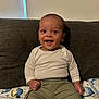 baby, child, smiling, happy, sitting, couch, clothing, white_shirt, pants, olive_green, face, portrait, indoor, cute, infant, furniture, blanket, sea_creatures, young_child, person