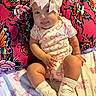 Chloe joined the competition — help win amazing prizes! baby, child, pink_bow, onesie, socks, shoes, pillow, bed, skull_pattern, rose_pattern, cute, smiling, tongue_out, indoor, infant, playful, colorful, soft_lighting, portrait, seated