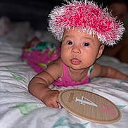 Chloe joined the competition — help win amazing prizes! baby, infant, child, hat, pink, bed, blanket, wooden_plaque, months, indoor, portrait, cute, expression, reaching_hand, soft_focus, clothing, face, person, lying_down, colorful