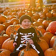 Riley Bea is registered to the contest to win money with this photo: baby, child, pumpkin, pumpkin_patch, autumn, fall, outdoor, smiling, black_clothing, hat, cute, seasonal, holiday, nature, sunlight, orange, festive, skeleton_costume, happy, sitting