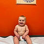 Tucker is registered to the contest to win money with this photo: baby, diaper, smiling, sitting, child, indoor, orange_wall, medical_table, bare_chest, happy, infant, feet, hands, face, head, portrait, human, room, wall_art, sports_stadium_map