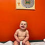 baby, child, diaper, smiling, sitting, orange_wall, medical_table, indoor, happy, cute, face, skin, barefoot, toes, head, person, room, artwork, stadium, photography