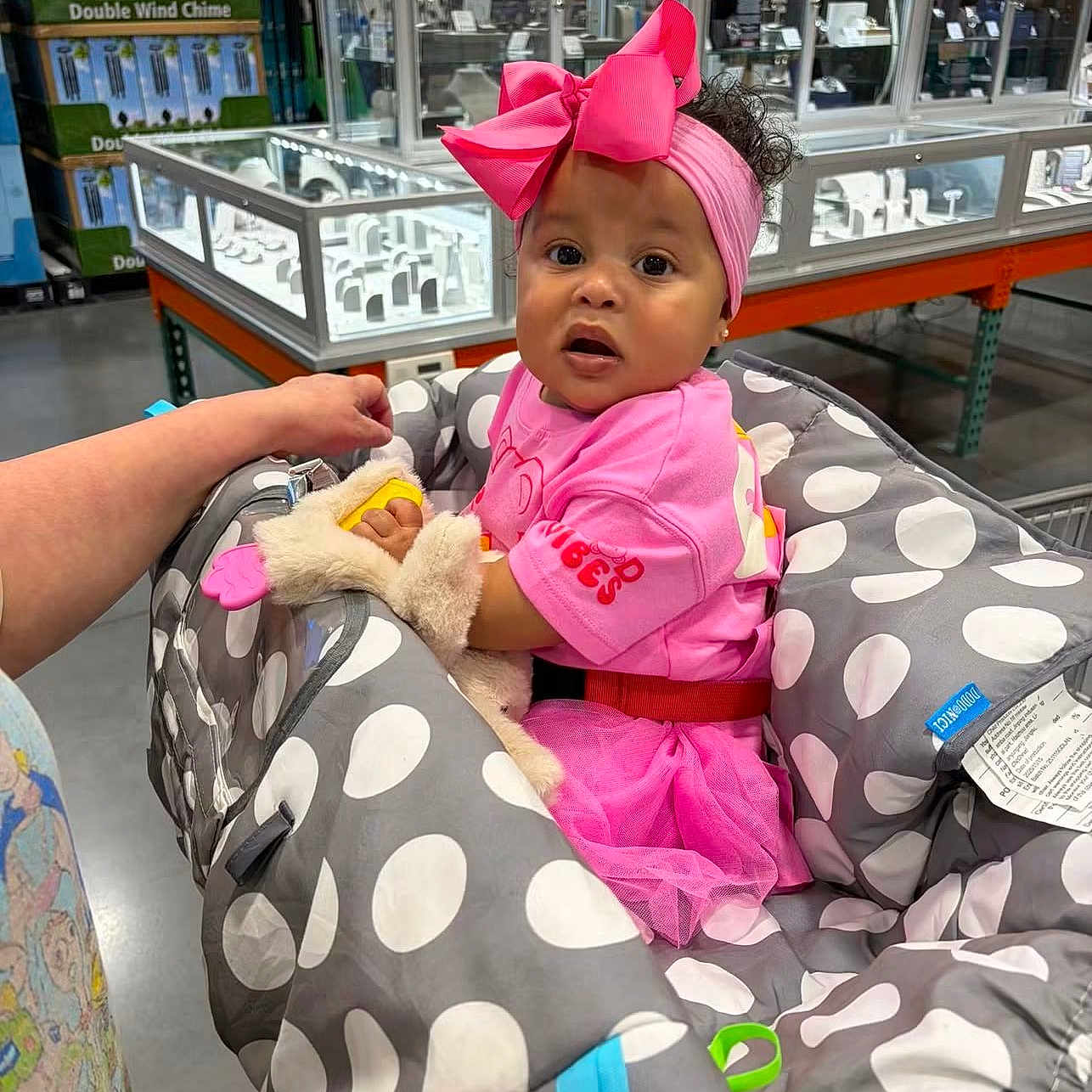 Sin Clair is registered to the contest to win money with this photo: baby, child, pink_clothing, headband, bow, baby_carrier, polka_dots, shopping_cart, store, display_case, curly_hair, hand, toddler, indoor, retail, person, cute, fashion, accessory, shopping