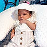 baby, infant, child, portrait, lying_down, sunhat, romper, white_clothing, smiling, hand_to_mouth, bed, pillow, blanket, bedroom, indoor, blue_wall, metal_headboard, buttoned_outfit, relaxed, cute