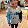 child, toddler, portrait, smiling, indoors, playroom, hat, floppy_hat, bluey_shirt, long_sleeves, pants, socks, shoes, wooden_floor, chair, table, toys, home, standing, face