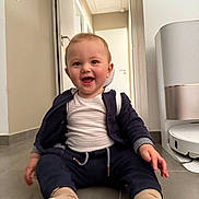 Dituan a rejoint le concours — aidez-le/la à gagner de superbes lots ! baby, child, smiling, sitting, floor, indoor, clothing, socks, jacket, white_shirt, hallway, door, air_purifier, robot_vacuum, tile_floor, happy, person, home, infant, cute