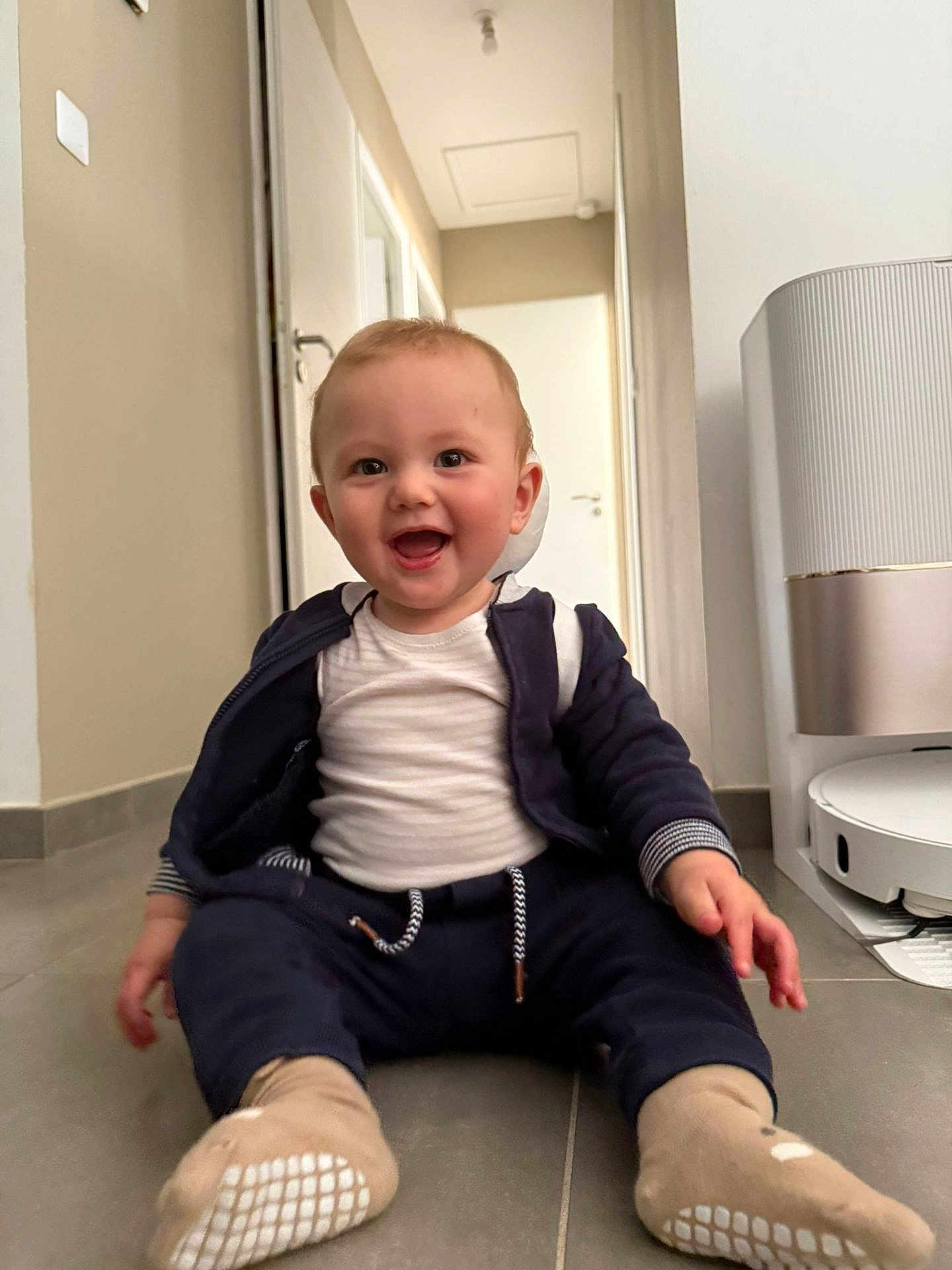 Dituan a rejoint le concours — aidez-le/la à gagner de superbes lots ! baby, child, smiling, sitting, floor, indoor, clothing, socks, jacket, white_shirt, hallway, door, air_purifier, robot_vacuum, tile_floor, happy, person, home, infant, cute