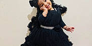 Anand is registered to the contest to win money with this photo: toddler, child, smile, black_dress, dress, pose, flooring, wood_floor, wall, happy, cute, girl, standing, footwear, gold_shoes, bracelet, curly_hair, indoors, portrait, fashion