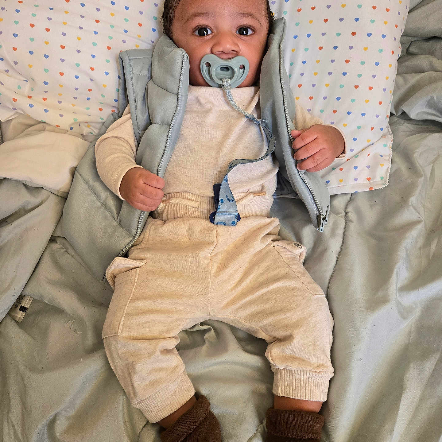 Ezrah is registered to the contest to win money with this photo: baby, bed, child, clothing, curious, cute, face, hand, heart_pattern, indoor, infant, lying_down, pacifier, pants, pillow, portrait, sleepwear, socks, soft_fabric, vest