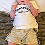 Tommy is registered to the contest to win money with this photo: baby, infant, child, cute, clothing, shirt, shorts, socks, blanket, bed, portrait, face, hands, feet, lying_down, indoor, young, curious, expression, cozy