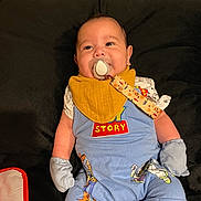 Ryan joined the competition — help win amazing prizes! baby, pacifier, bib, mittens, toy_story, blue_outfit, couch, black_background, smiling, infant, indoor, child, cute, happy, relaxed, clothing, face, person, sitting, home