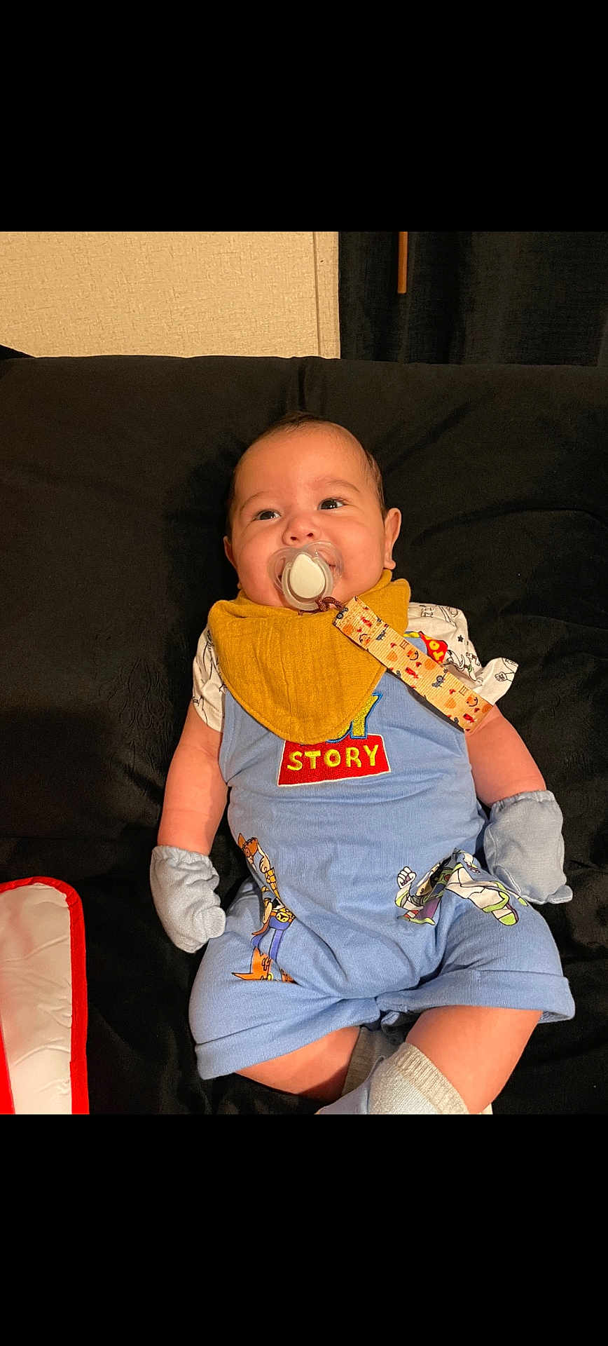 Ryan joined the competition — help win amazing prizes! baby, pacifier, bib, mittens, toy_story, blue_outfit, couch, black_background, smiling, infant, indoor, child, cute, happy, relaxed, clothing, face, person, sitting, home